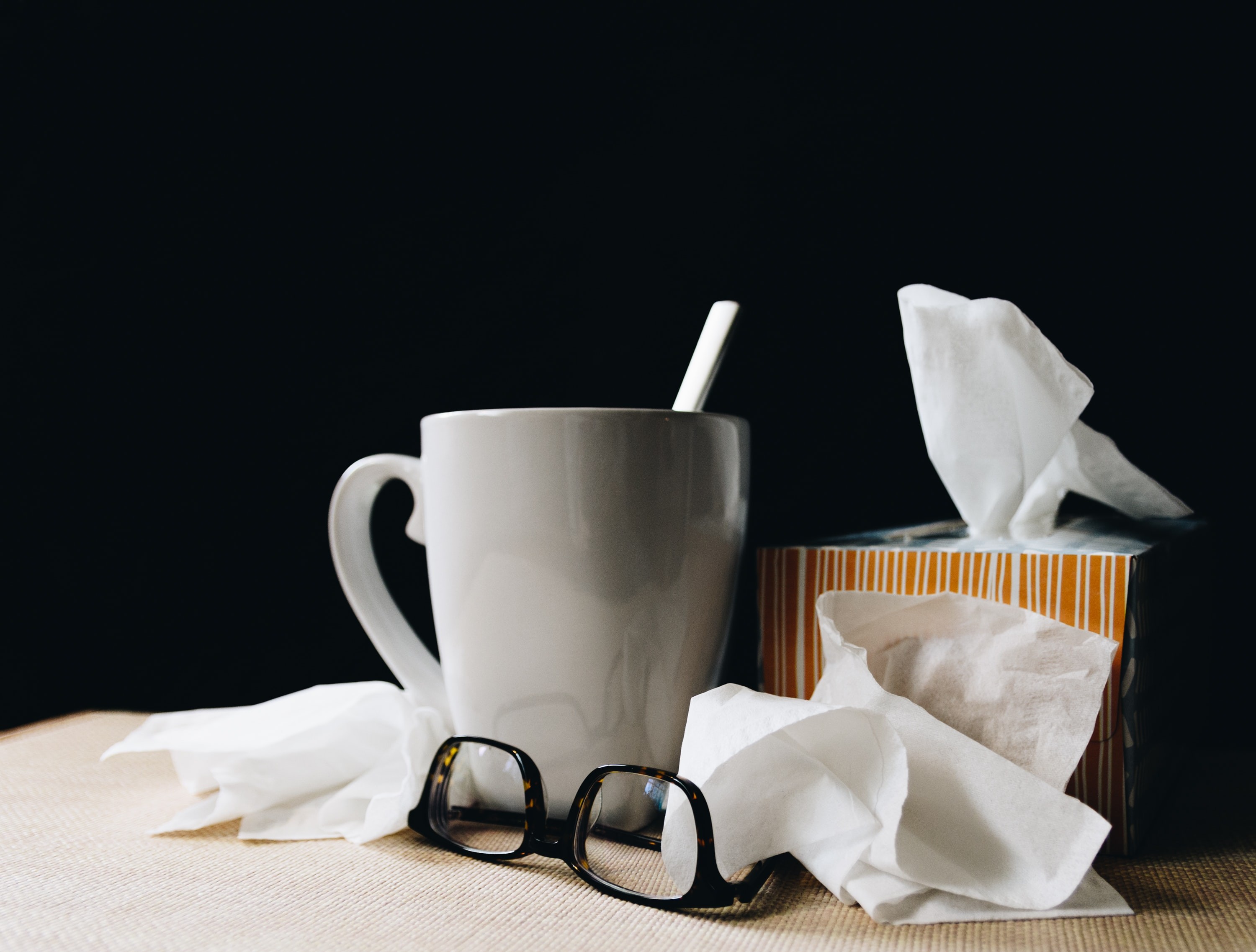 photo of a paid of glasses and a mug, beside a box of tissues and some used tissues