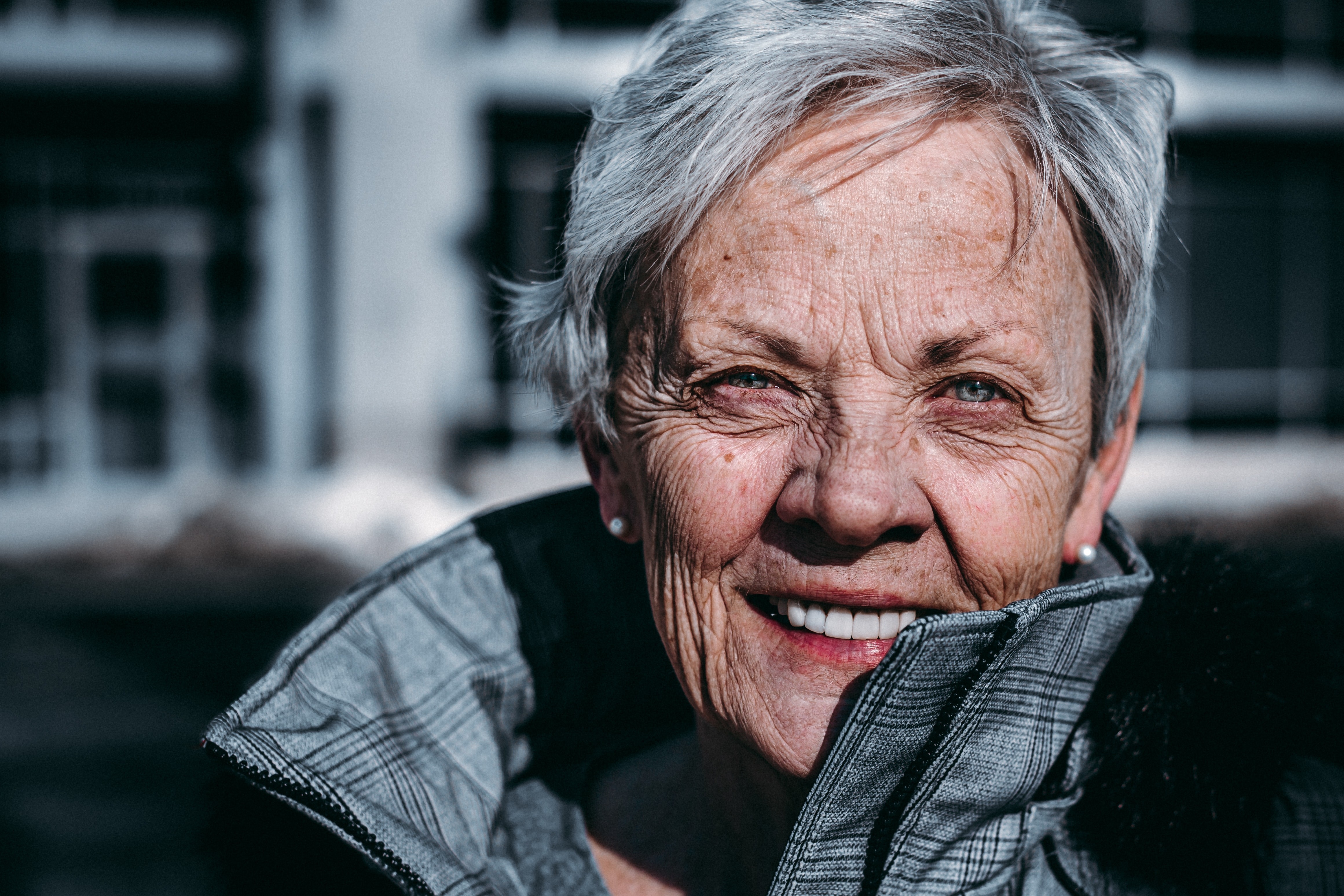 photo of a smiling, older woman, stood outside in the sun with a light breeze blowing her hair