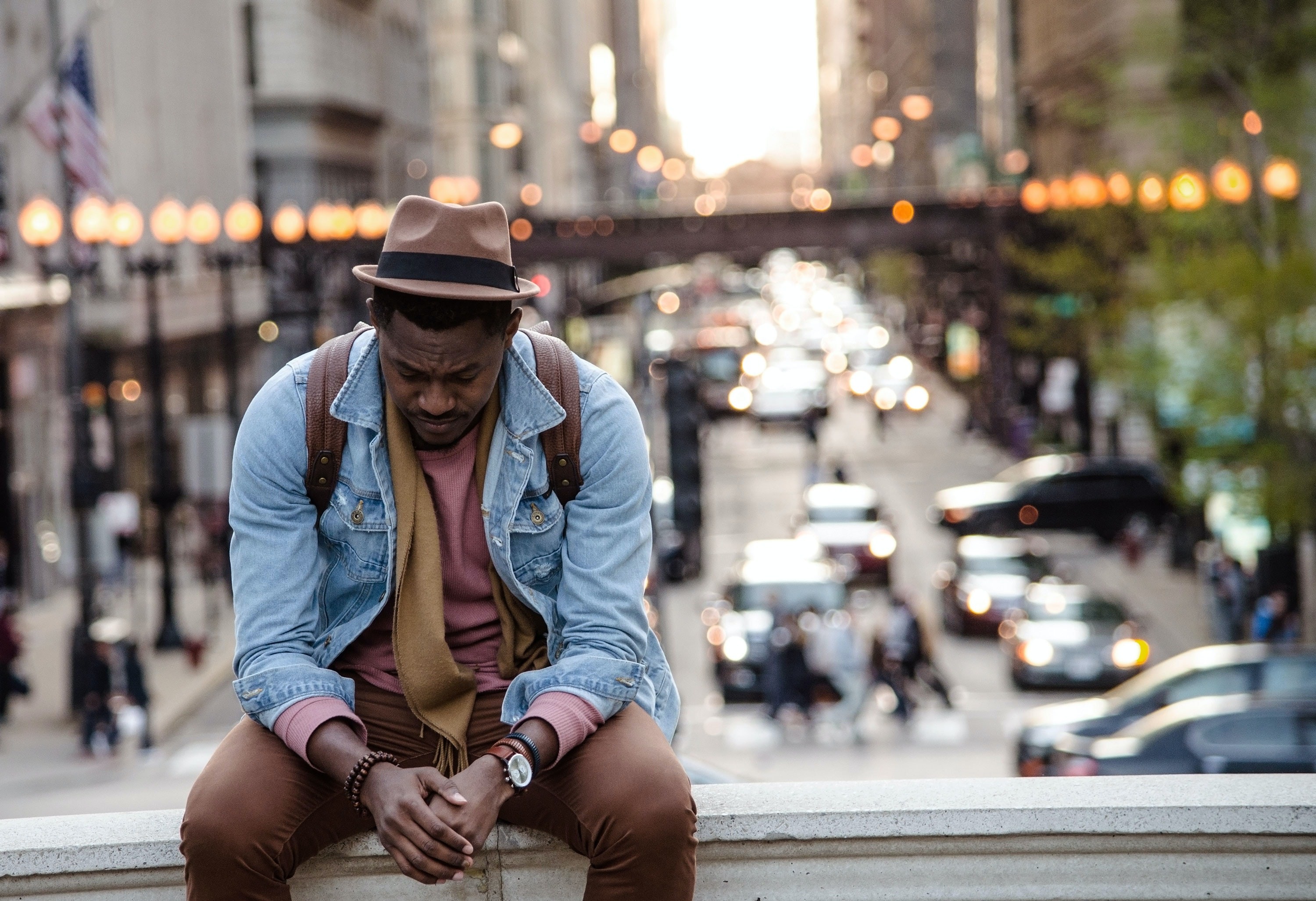 photo of a man sat outside, alone, looking down sadly, with a busy city behind him
