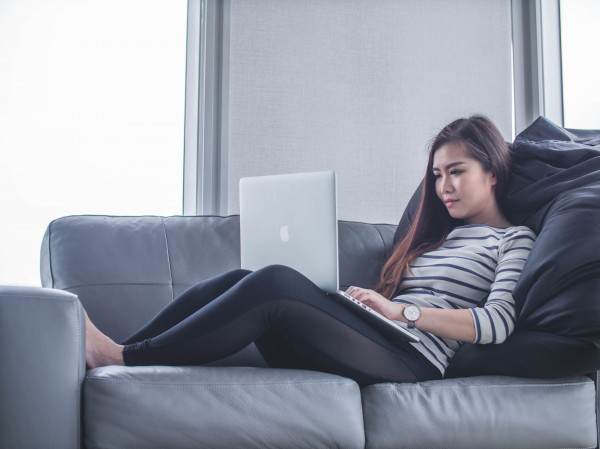photo of a woman slouched on a sofa, using her laptop, supported by cushions